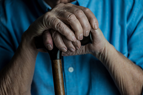 Close up of elderly hands resting on top of a walking cane